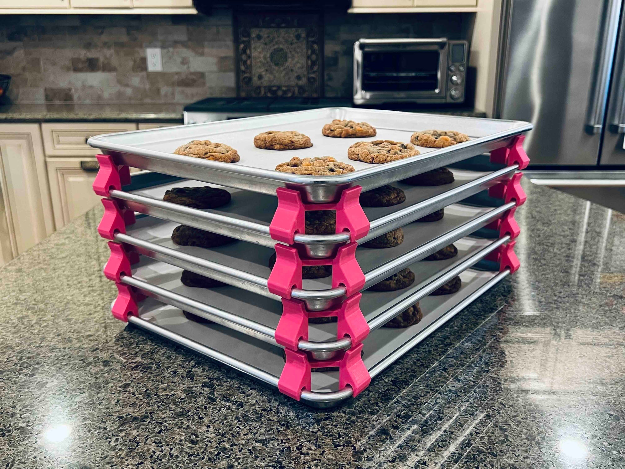 3D printed baking sheet organizers at an angle in hot pink, neatly holding and organizing multiple cookie sheets to save counter space in the kitchen.