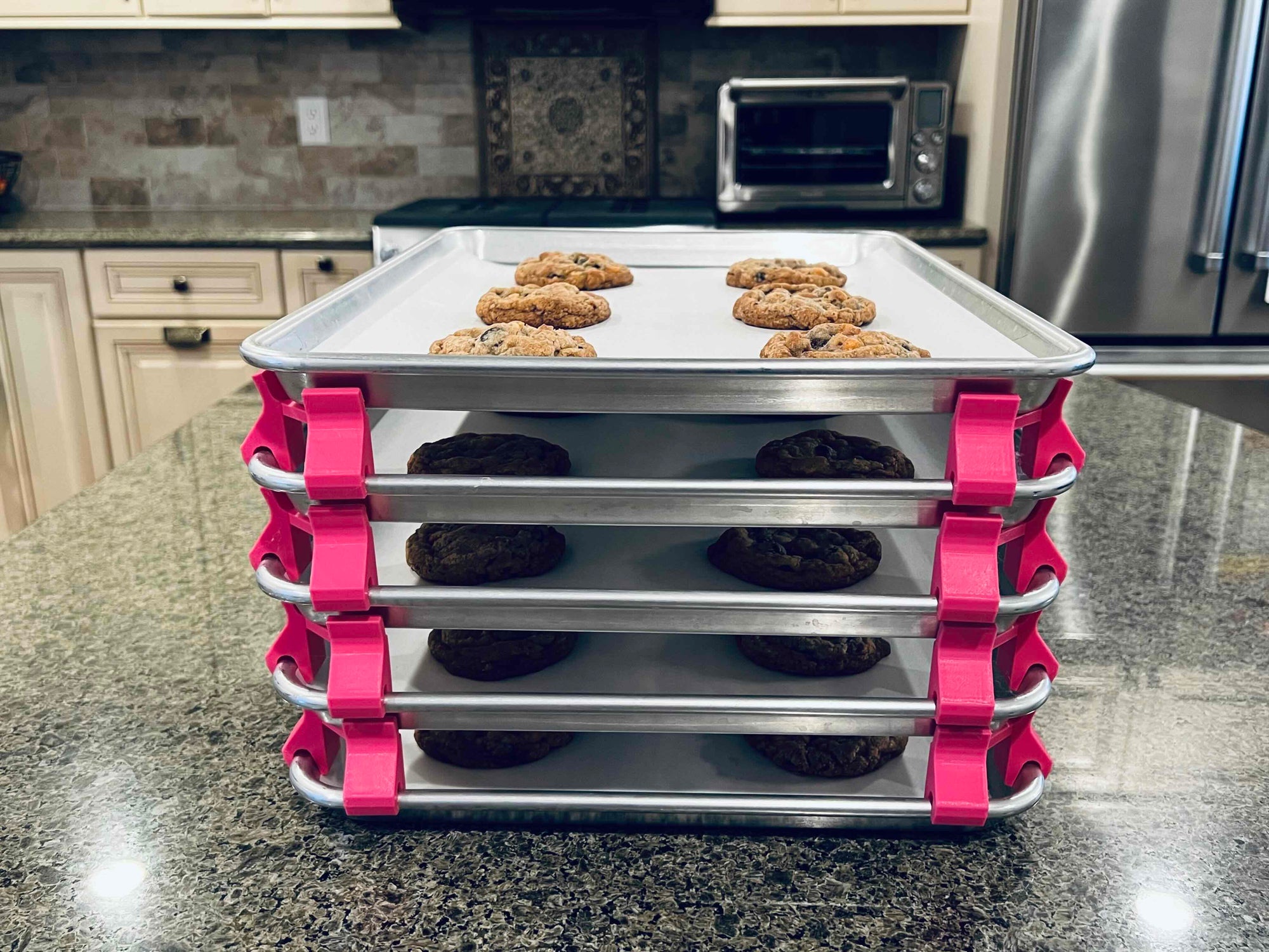 3D printed baking sheet organizers from the front in hot pink, neatly holding and organizing multiple cookie sheets to save counter space in the kitchen.