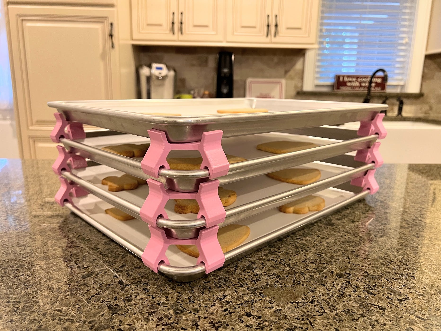 3D printed baking sheet organizers at an angle in pink, neatly holding and organizing multiple cookie sheets to save counter space in the kitchen.