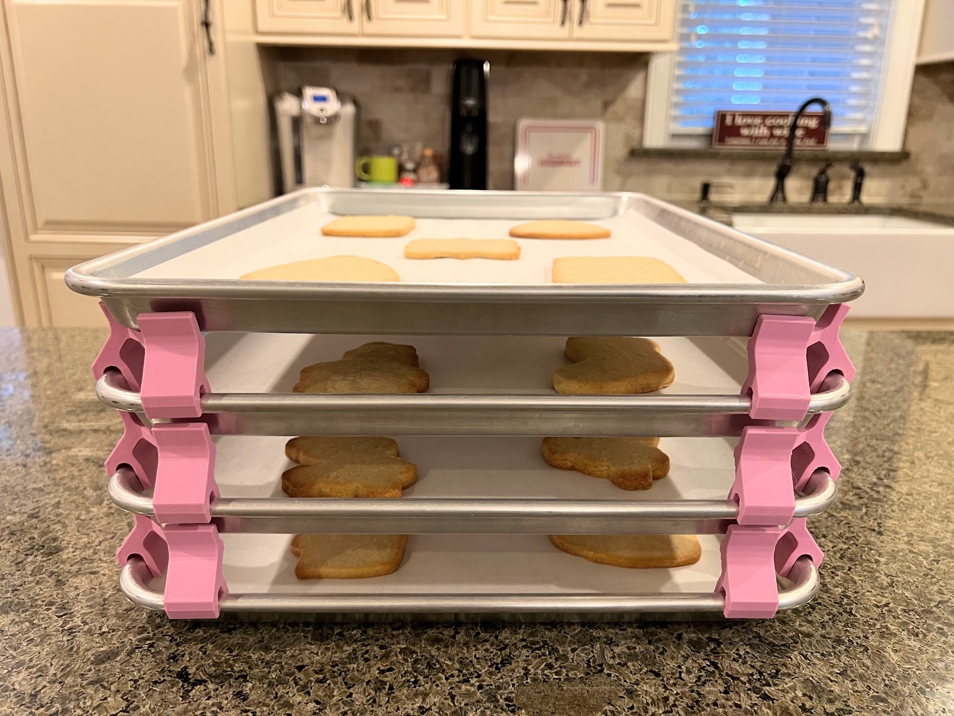 3D printed baking sheet organizers from the front in pink, neatly holding and organizing multiple cookie sheets to save counter space in the kitchen.