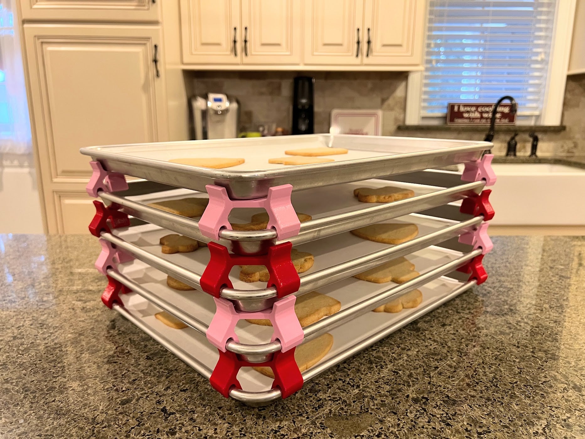 3D printed baking sheet organizers in alternating pink and red colors, neatly holding and organizing multiple cookie sheets to save counter space in the kitchen.