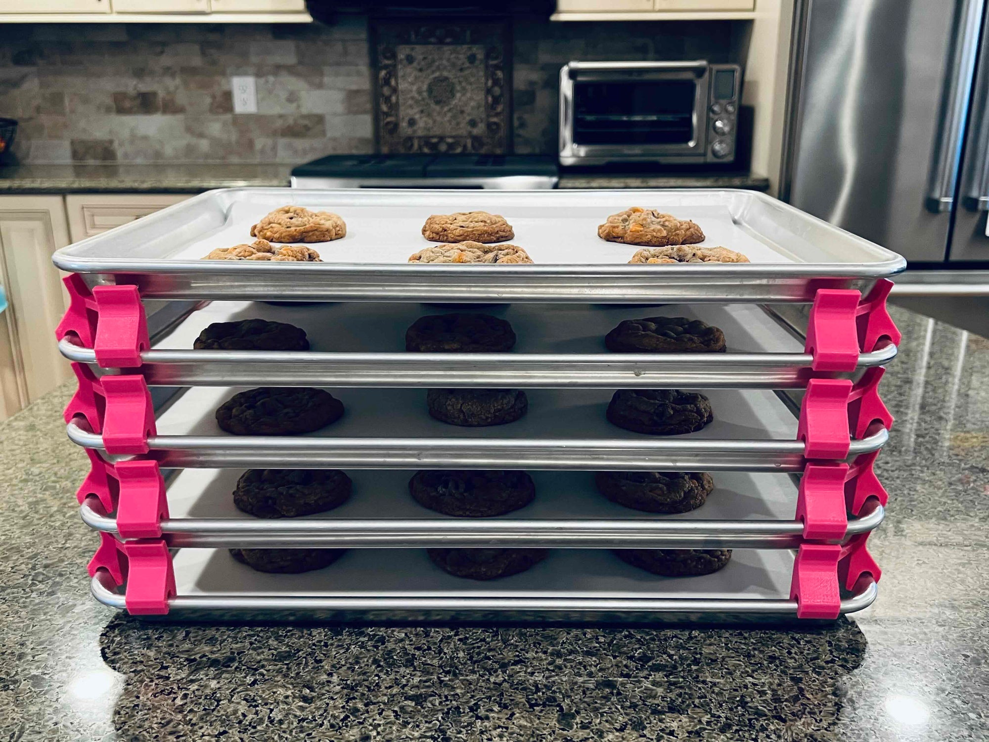 3D printed baking sheet organizers from the side in hot pink, neatly holding and organizing multiple cookie sheets to save counter space in the kitchen.