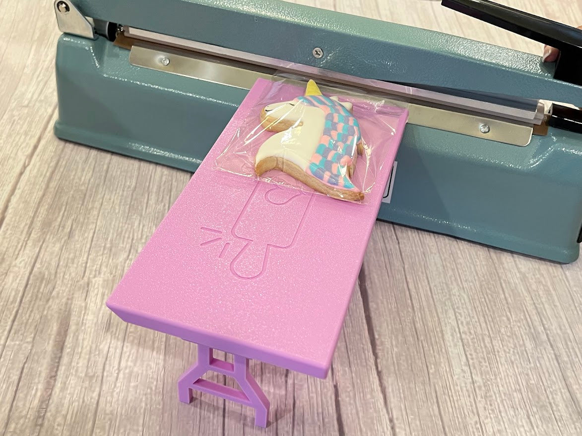 Lavender Heat Sealer Table in the long position with a unicorn cookie on it.