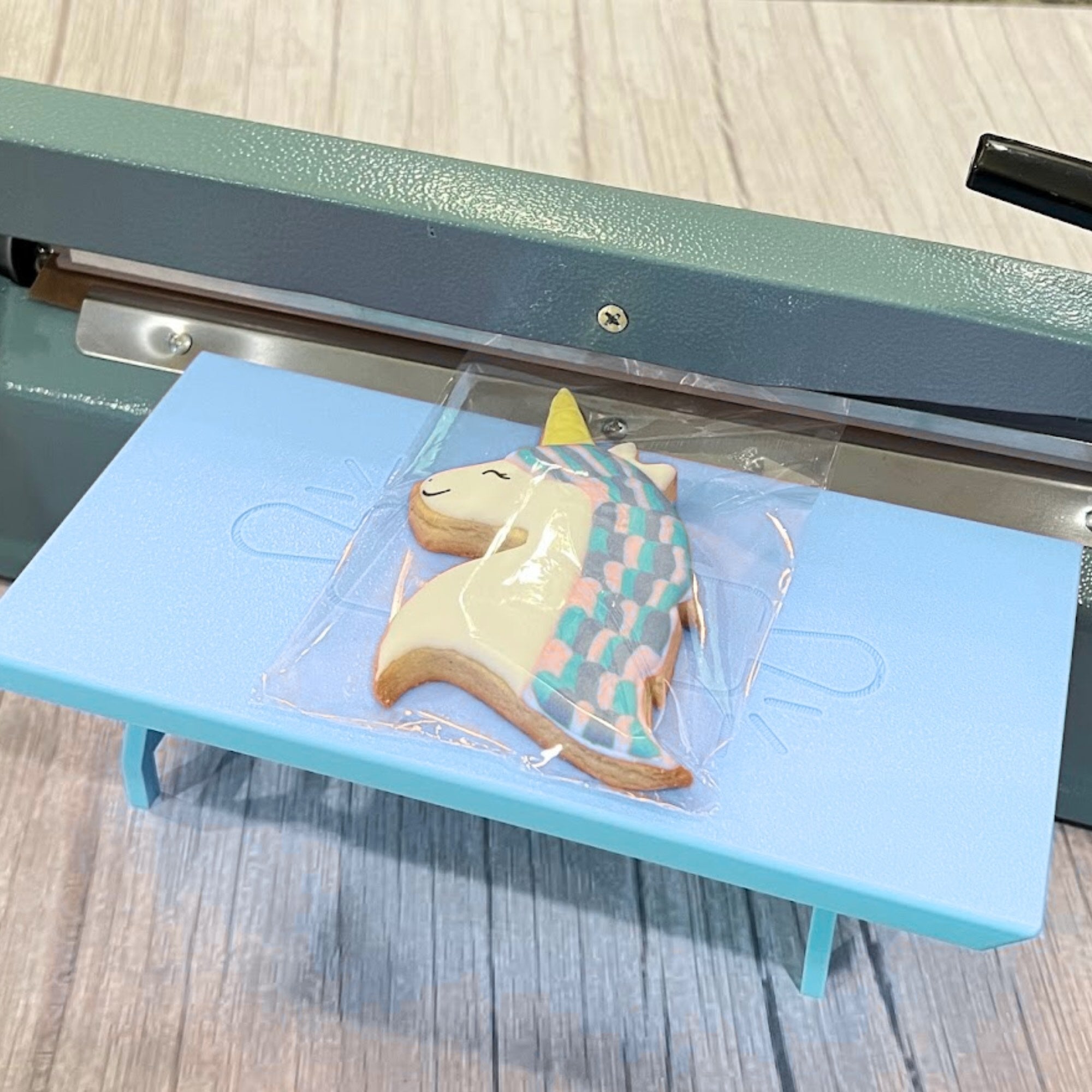 Light Blue Heat Sealer Table in the wide position with a unicorn cookie on it.